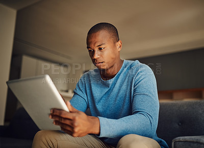 Buy stock photo Shot of a handsome young man using a digital tablet at home