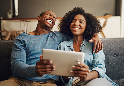 Buy stock photo Shot of a young couple laughing while using a digital tablet together at home