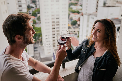 Buy stock photo Cropped shot of an attractive young couple drinking wine on a rooftop looking over the city