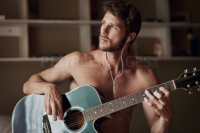Buy stock photo Cropped shot of a handsome young man playing a guitar at home