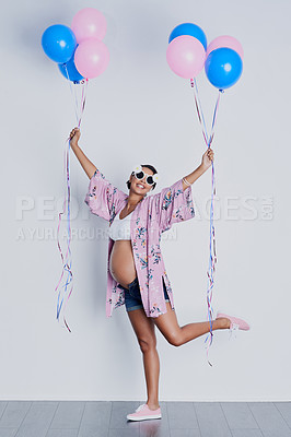 Buy stock photo Studio shot of a beautiful young pregnant woman holding blue and pink balloons against a gray background