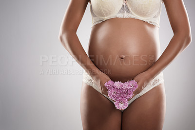 Buy stock photo Studio shot of an unrecognizable pregnant woman holding flowers against a gray background