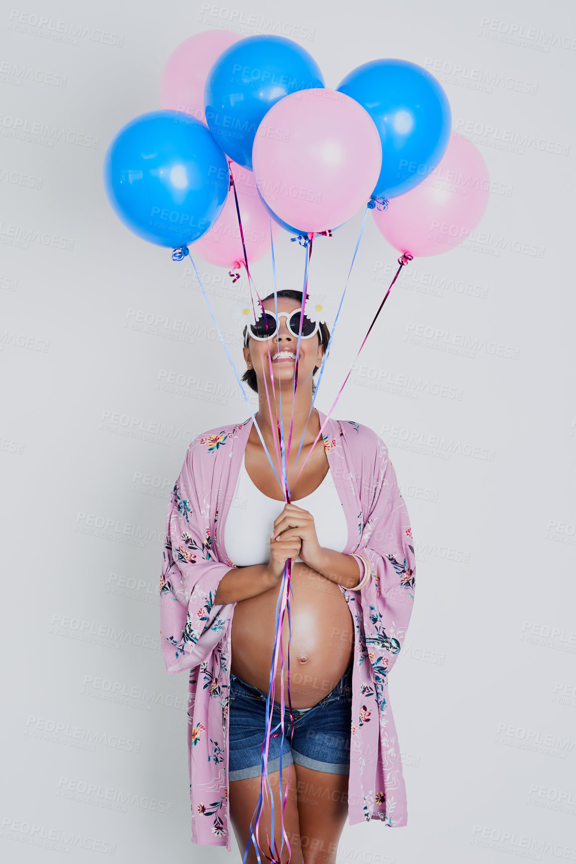 Buy stock photo Studio shot of a beautiful young pregnant woman holding blue and pink balloons against a gray background