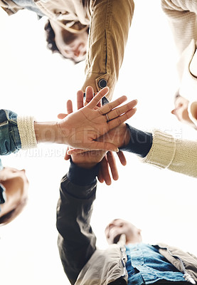 Buy stock photo Low angle shot of a group of young friends forming a huddle with their hands together outside during the day