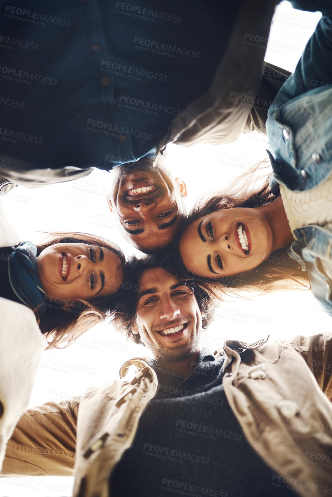 Buy stock photo Low angle portrait of a group of young friends huddled together while looking down at the camera outside during the day