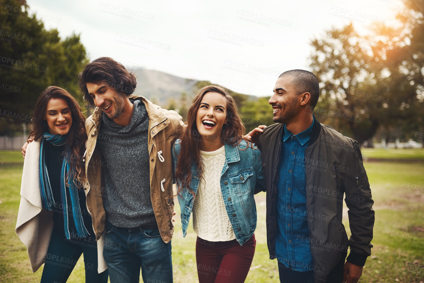 Buy stock photo Shot of a group of cheerful young friends huddled together while walking in a park outside during the day