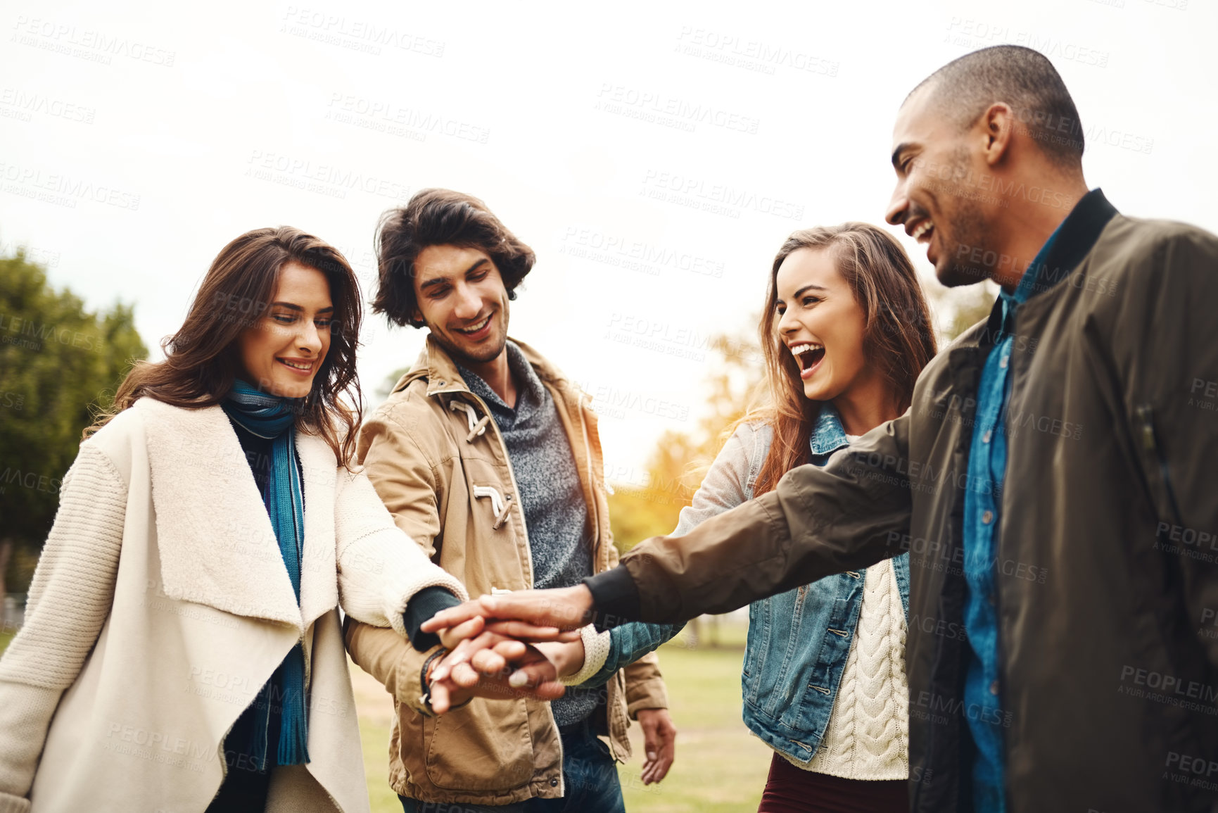 Buy stock photo Shot of a group of cheerful young friends forming a huddle with their hands together outside during the day