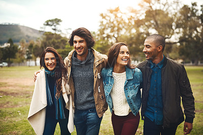 Buy stock photo Portrait of a group of cheerful young friends huddled together while walking in a park outside during the day