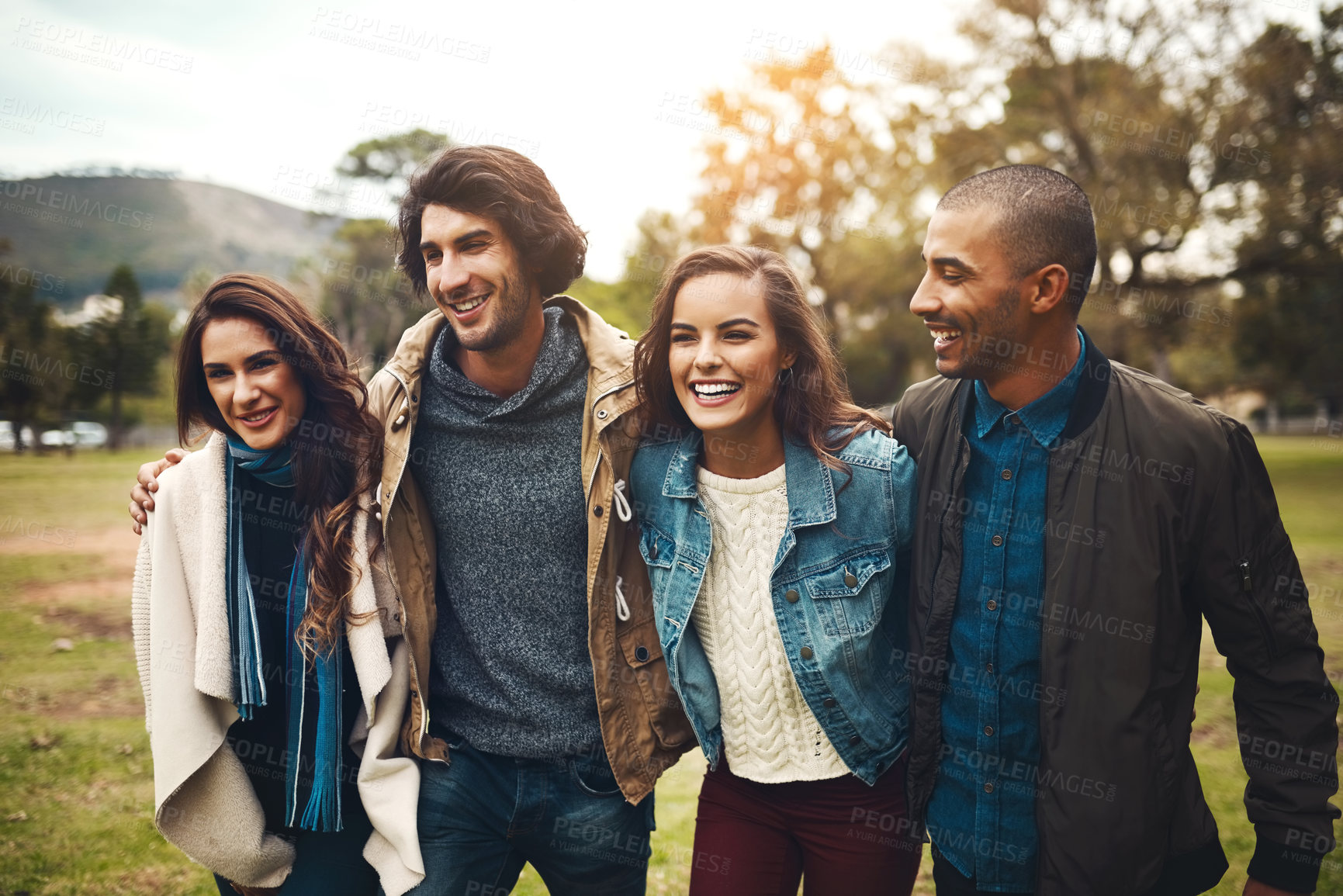 Buy stock photo Portrait of a group of cheerful young friends huddled together while walking in a park outside during the day