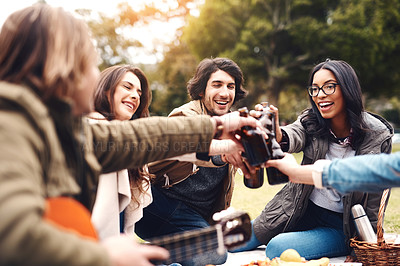 Buy stock photo Shot of a group of cheerful young friends having a picnic together while celebrating with a toast outside in a park during the day