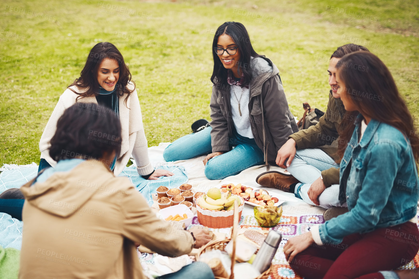 Buy stock photo Shot of a group of cheerful young friends having a picnic together outside in a park during the day
