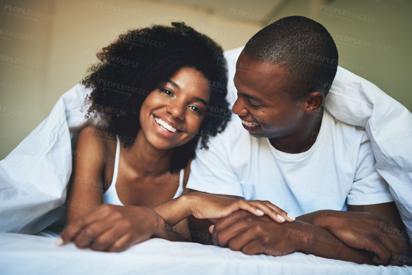 Buy stock photo Portrait of a happy young couple relaxing under a duvet in their bedroom