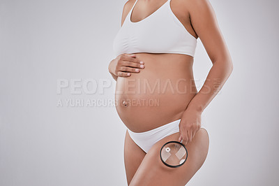 Buy stock photo Cropped studio shot of a pregnant woman holding a magnifying glass to her thighs against a gray background