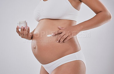 Buy stock photo Cropped studio shot of a pregnant woman applying moisturizer to her belly against a gray background