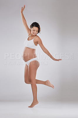 Buy stock photo Studio shot of a beautiful young pregnant woman standing with her arms outstretched against a gray background