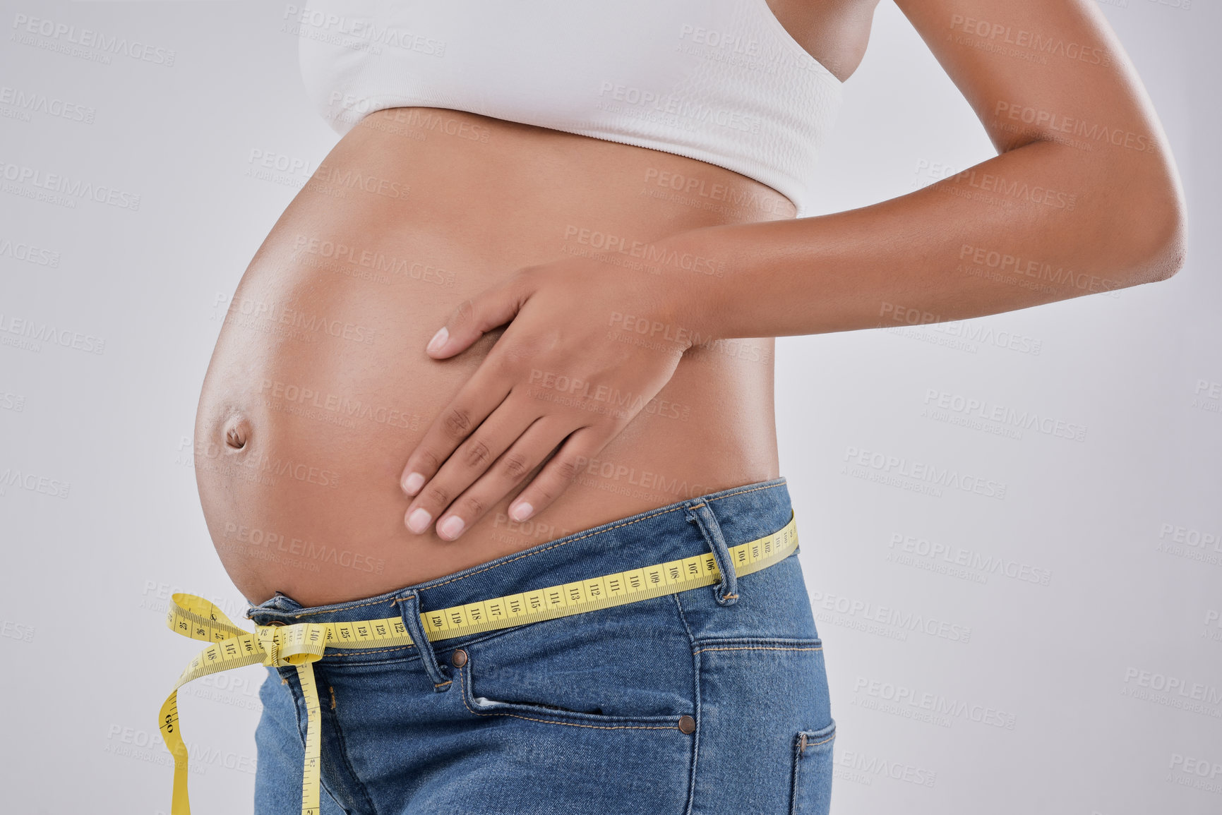 Buy stock photo Pregnancy, measuring tape and jeans with woman in studio for belly size, gynecology and maternal. Prenatal health, growth and development with body of pregnant person on white background for tracking