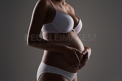 Buy stock photo Cropped studio shot of a pregnant woman making a heart shape on her belly against a gray background