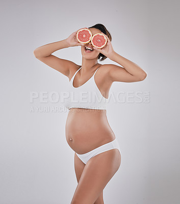 Buy stock photo Studio shot of a beautiful young pregnant woman covering her eyes with grapefruit against a gray background