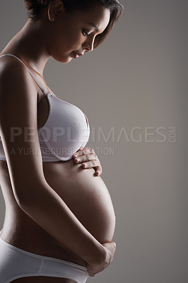 Buy stock photo Studio shot of a beautiful young pregnant woman posing in underwear against a gray background