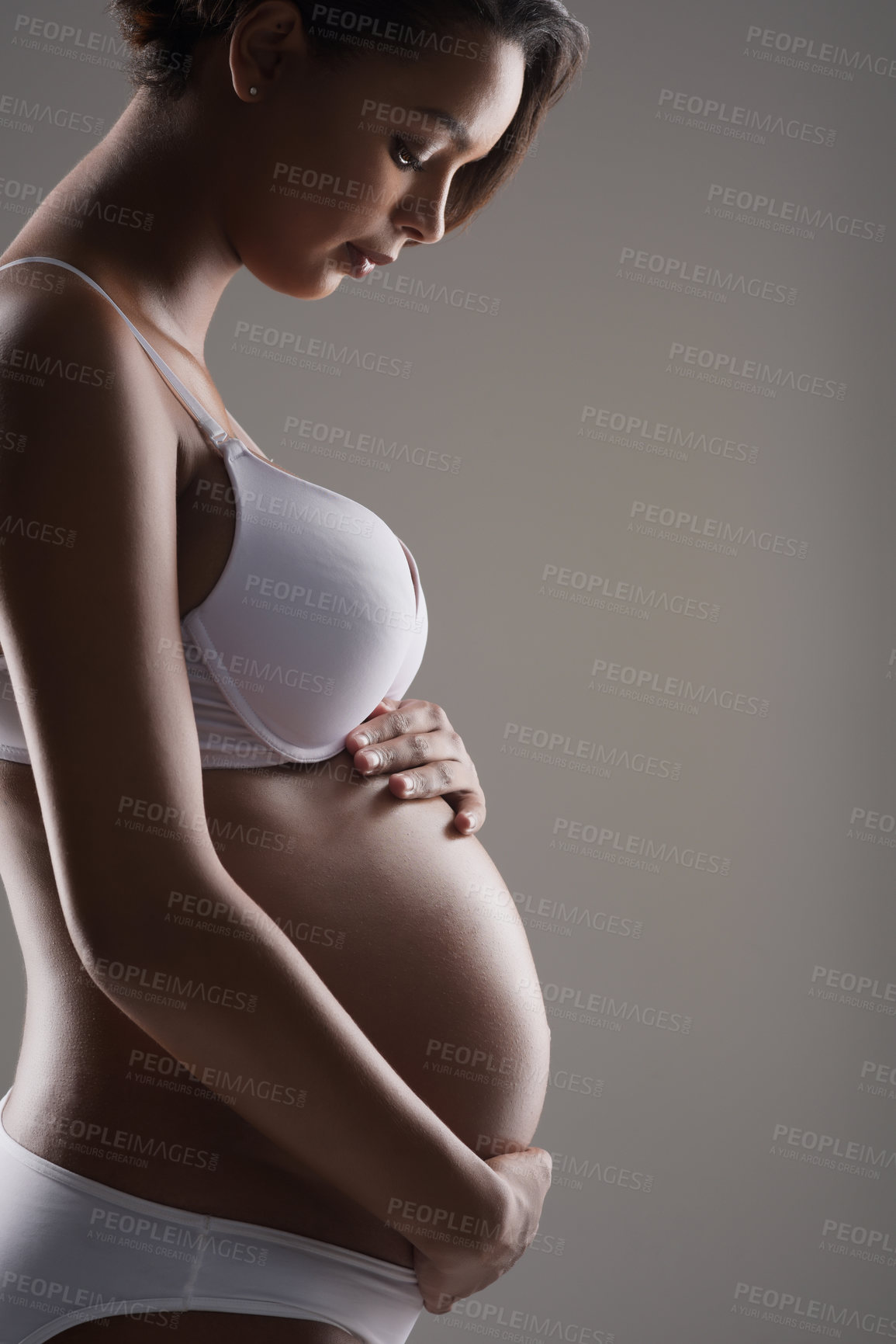 Buy stock photo Studio shot of a beautiful young pregnant woman posing in underwear against a gray background