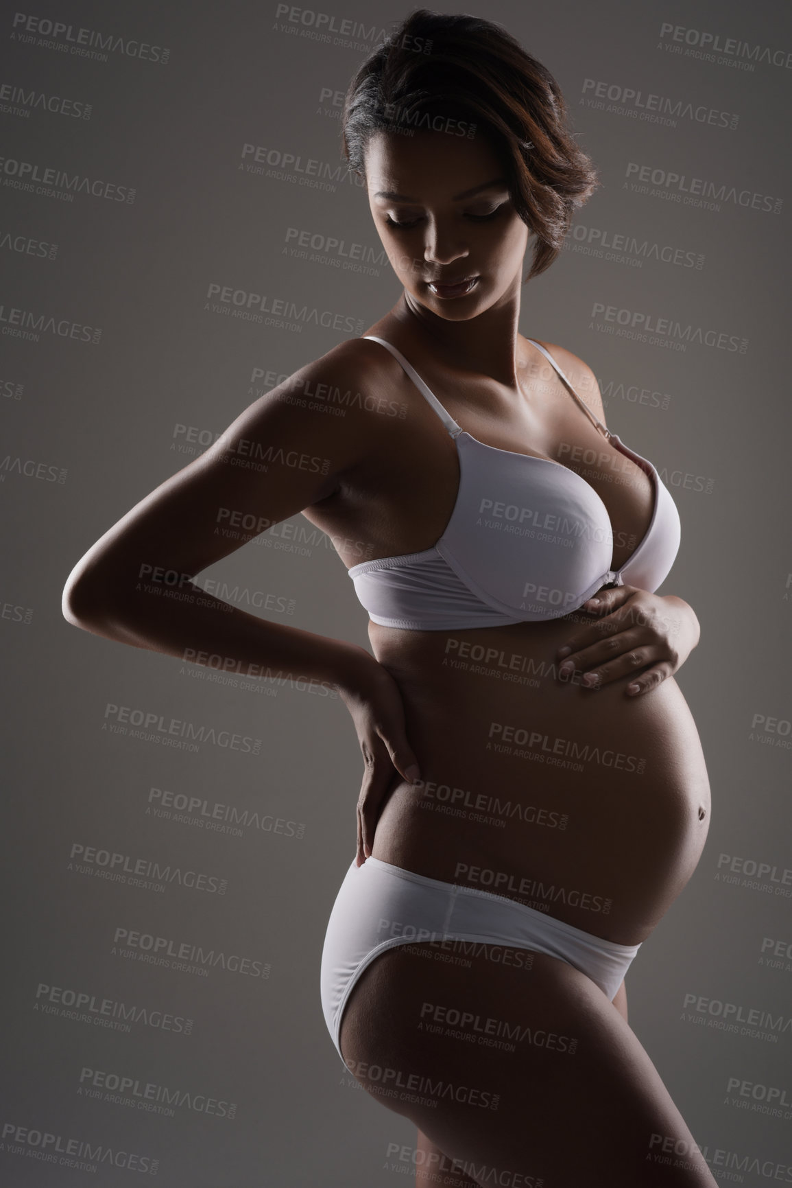 Buy stock photo Studio shot of a beautiful young pregnant woman posing in underwear against a gray background