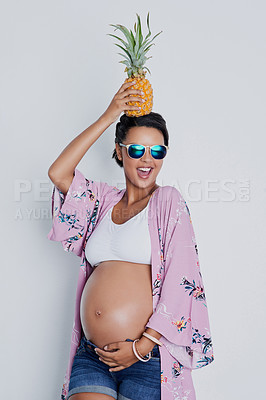 Buy stock photo Studio shot of a beautiful young pregnant woman holding a pineapple on top of her head against a gray background