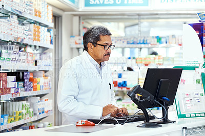 Buy stock photo Shot of a mature pharmacist working on a computer in a chemist