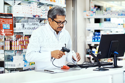 Buy stock photo Shot of a mature pharmacist scanning a product on a computer in a chemist