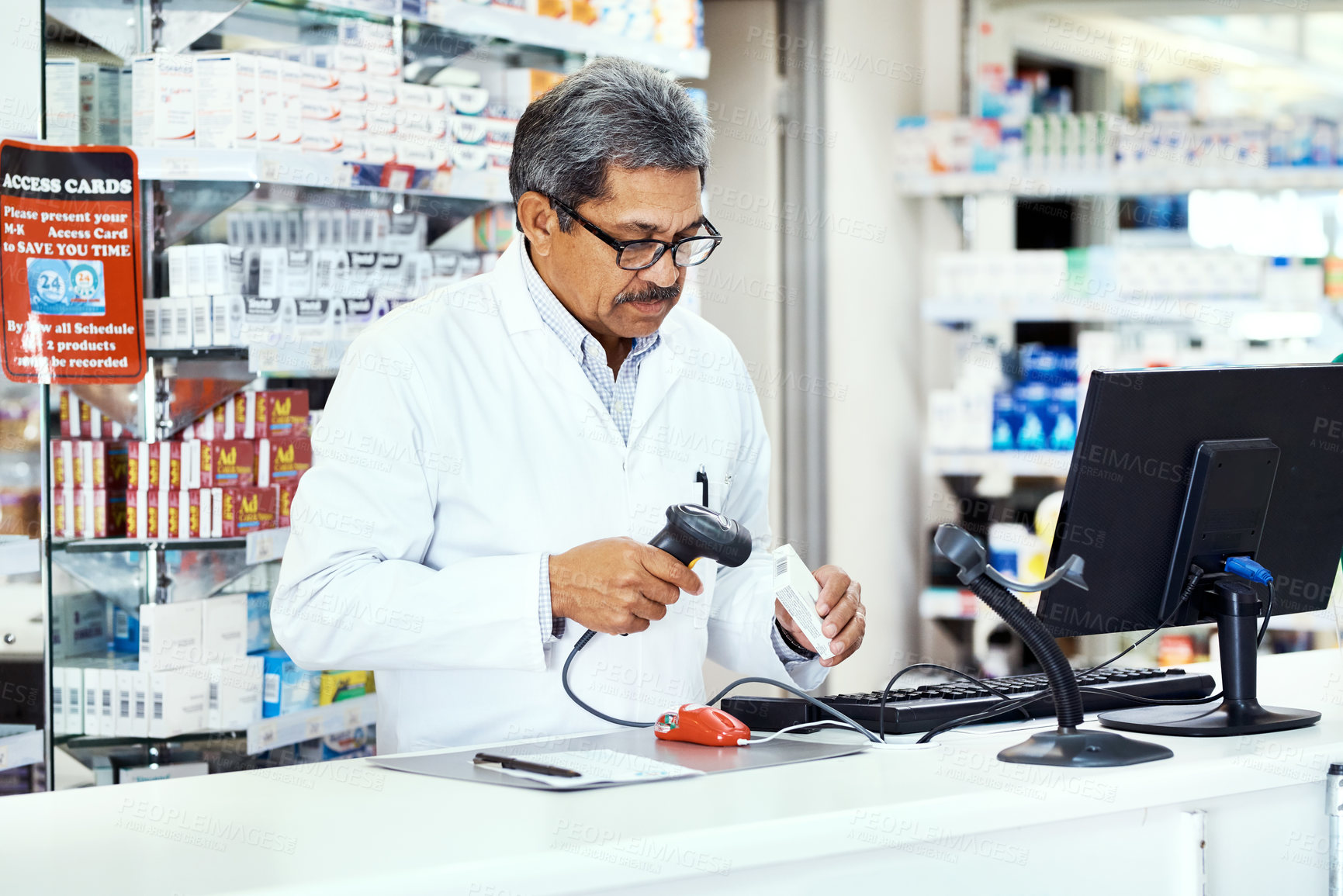 Buy stock photo Shot of a mature pharmacist scanning a product on a computer in a chemist