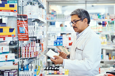 Buy stock photo Shot of a mature pharmacist using a digital tablet while working in a chemist