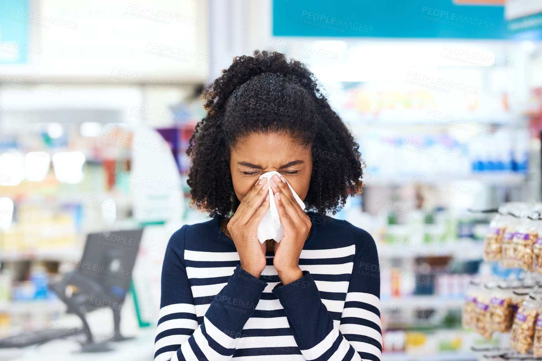 Buy stock photo Shot of a young woman blowing her nose in a pharmacy