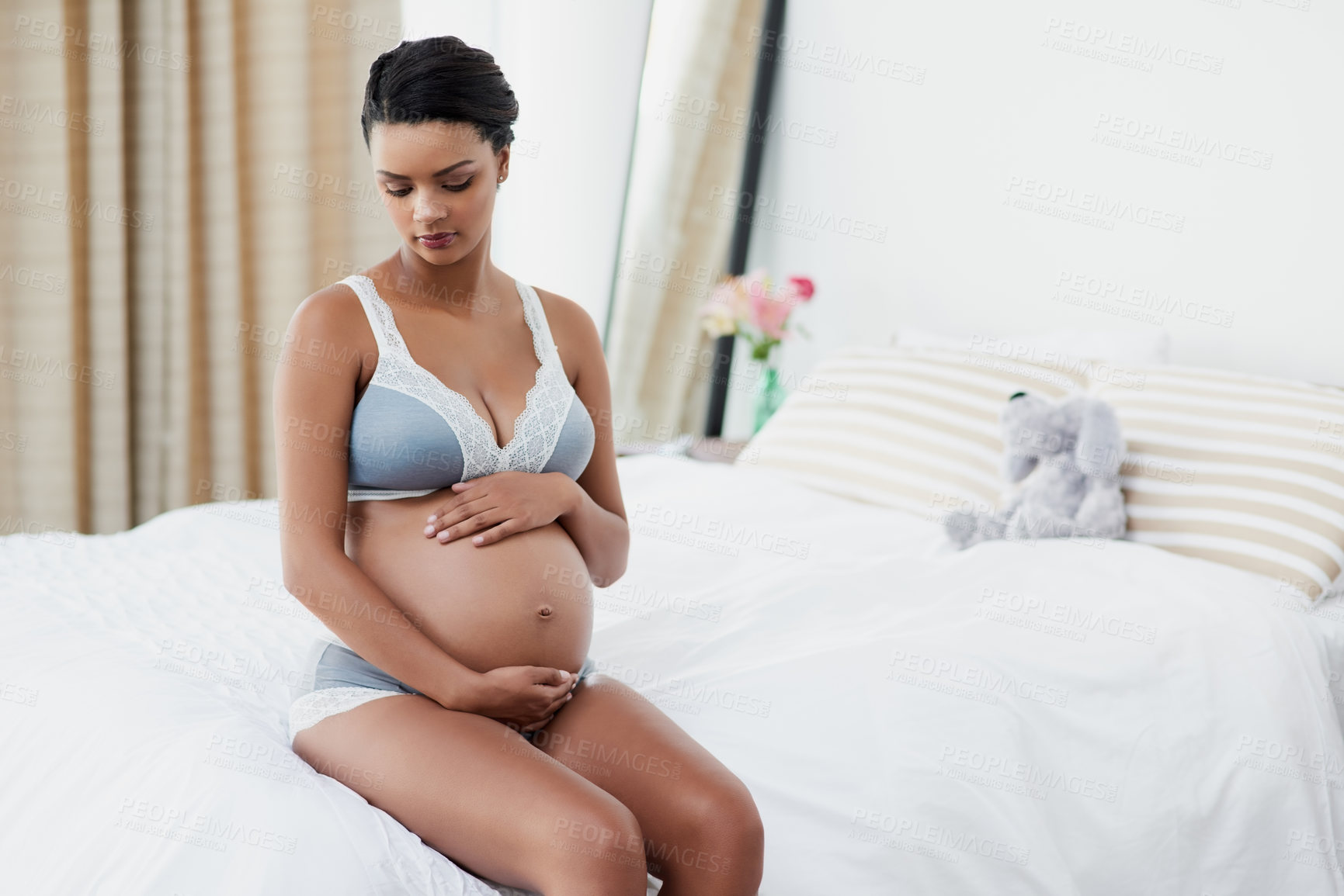 Buy stock photo Shot of a pregnant young woman sitting on her bed at home