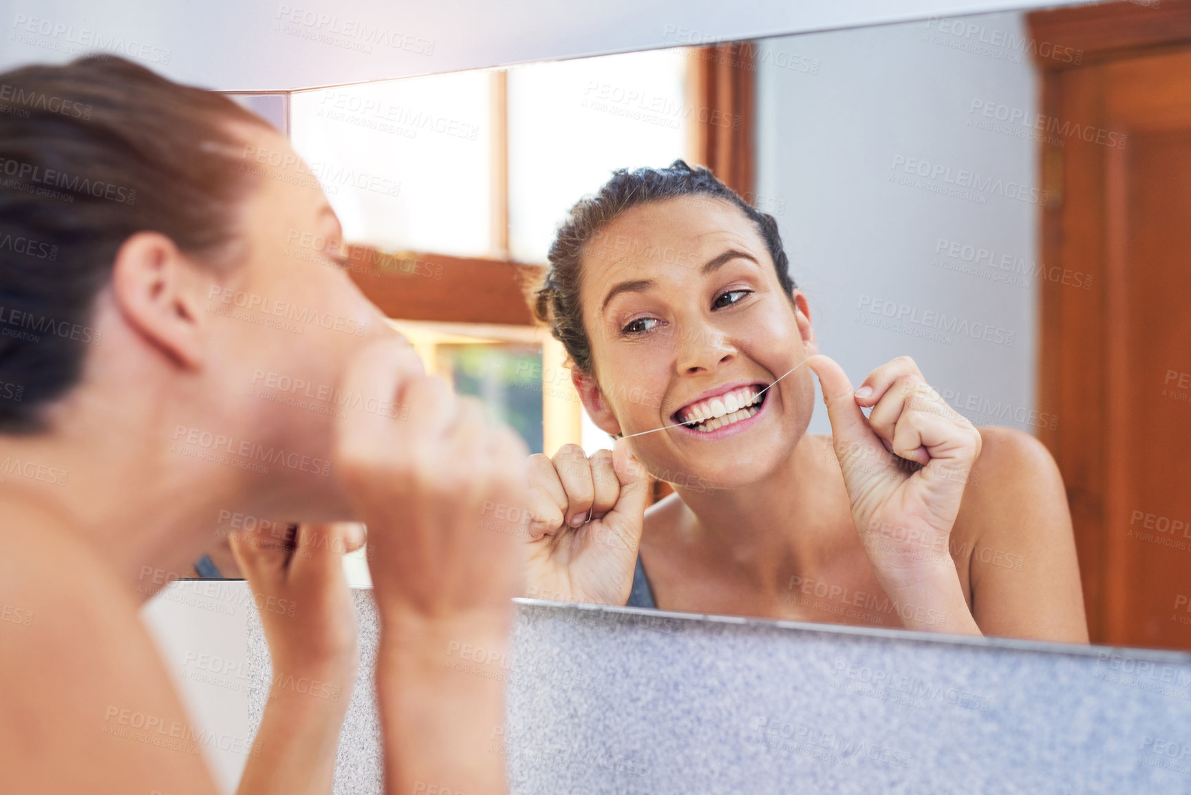 Buy stock photo Shot of an attractive young woman flossing her teeth in the bathroom