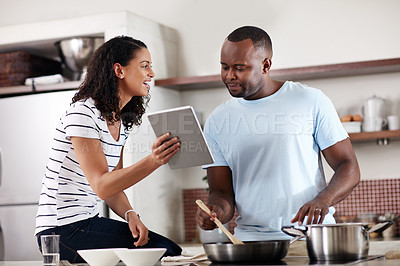 Buy stock photo Cropped shot of a young married couple using a tablet while cooking together in the kitchen at home