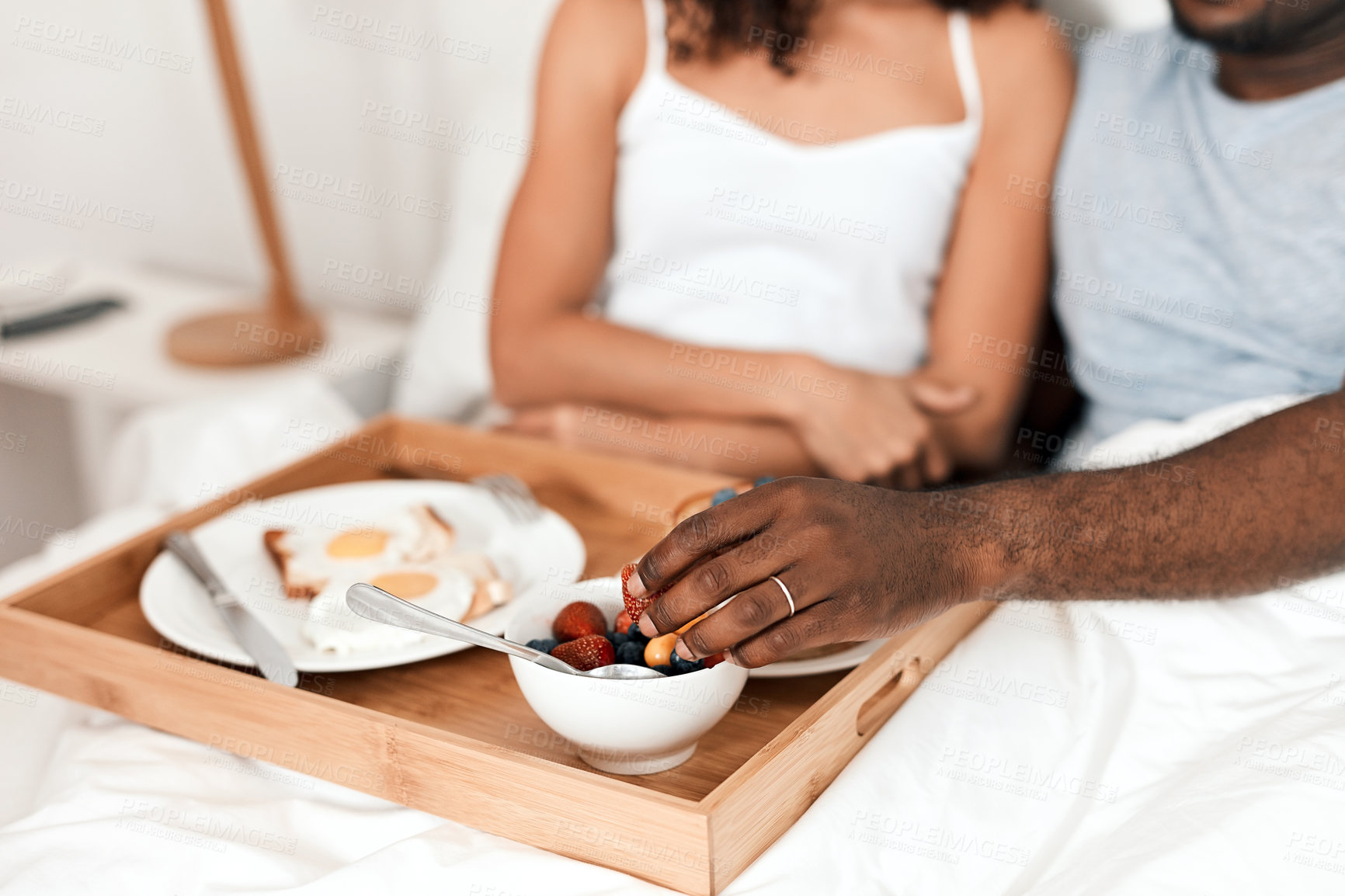 Buy stock photo Shot of an unrecognizable couple enjoying breakfast in bed together at home during the day
