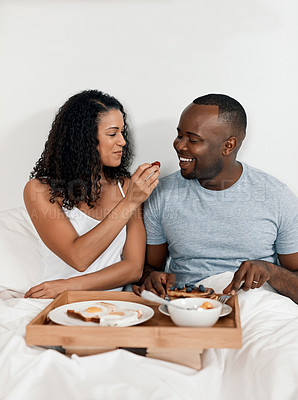 Buy stock photo Shot of a cheerful young couple enjoying breakfast in bed together at home during the day
