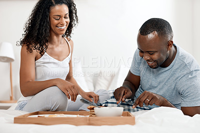 Buy stock photo Shot of a cheerful young couple enjoying breakfast in bed together at home during the day