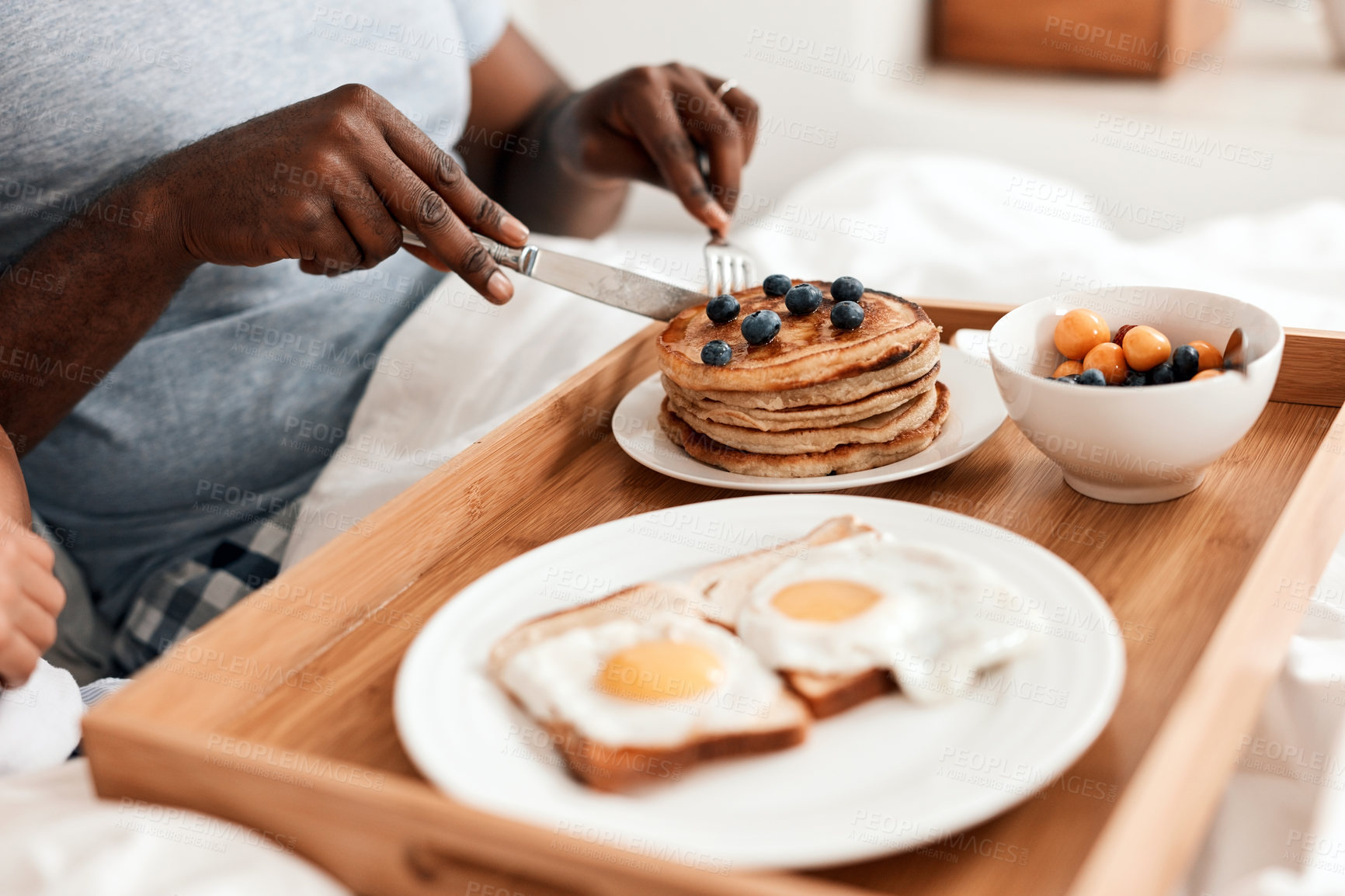 Buy stock photo Shot of an unrecognizable couple enjoying breakfast in bed together at home during the day