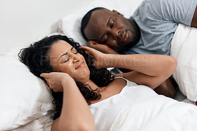 Buy stock photo Shot of an uncomfortable looking young woman holding her ears closed because of her husband's snoring in bed at home