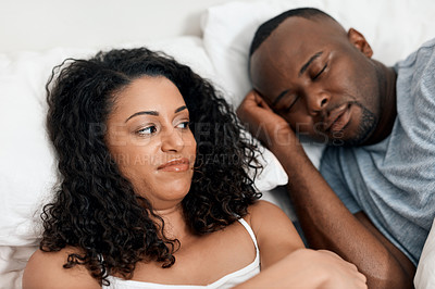Buy stock photo Shot of a irritated looking young woman lying in bed with her husband and trying to get some sleep but can't due to his snoring