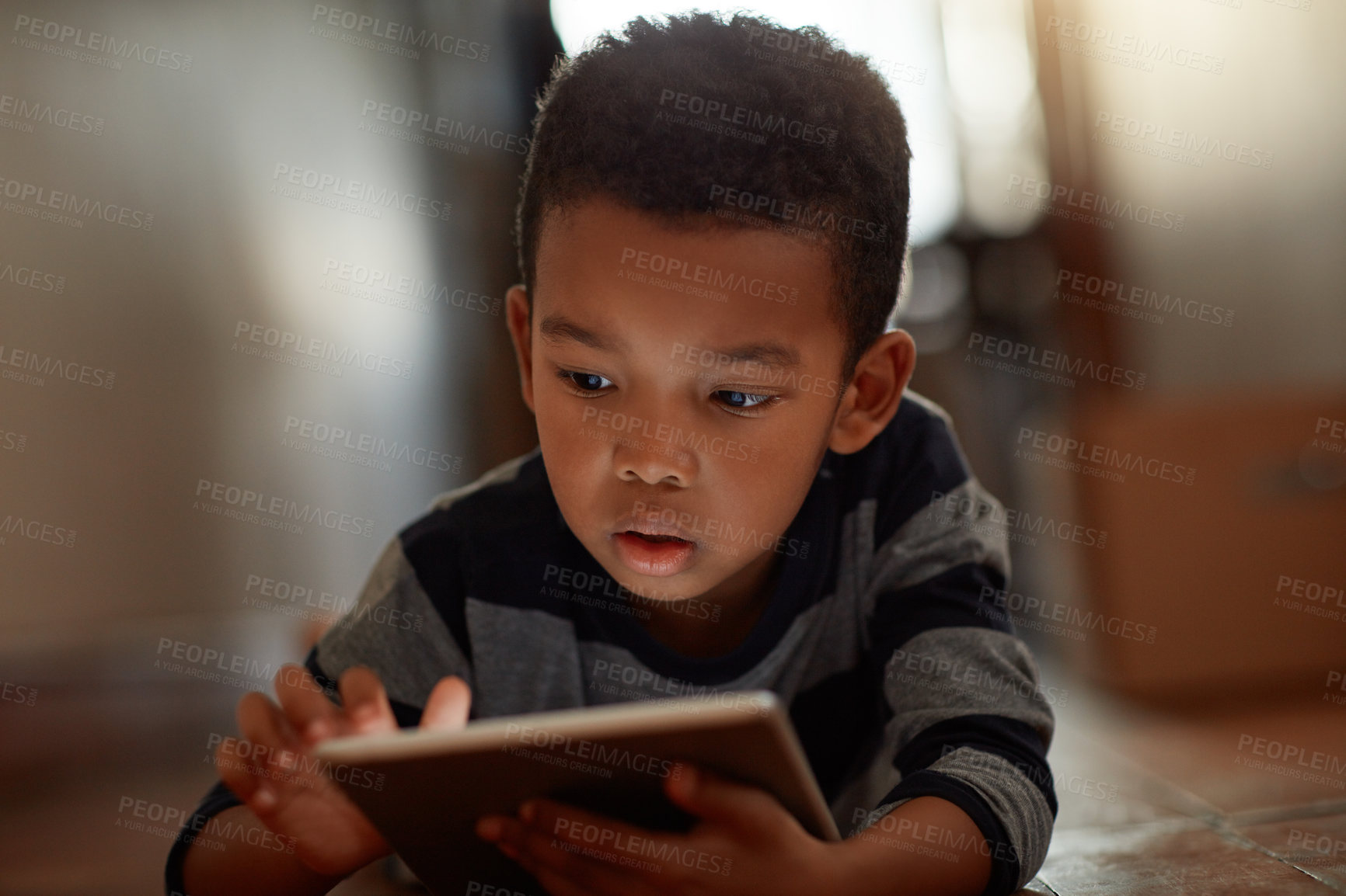 Buy stock photo Shot of a young boy using his digital tablet while lying on the floor at home