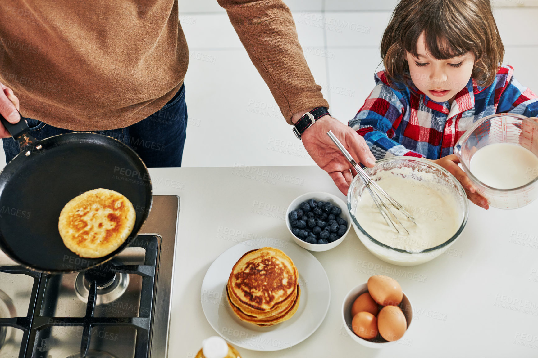 Buy stock photo High angle shot of an adorable little boy making pancakes with his unrecognizable father in the kitchen at home