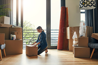 Buy stock photo Shot of a focused middle aged woman packing out a box at her new home inside during the day