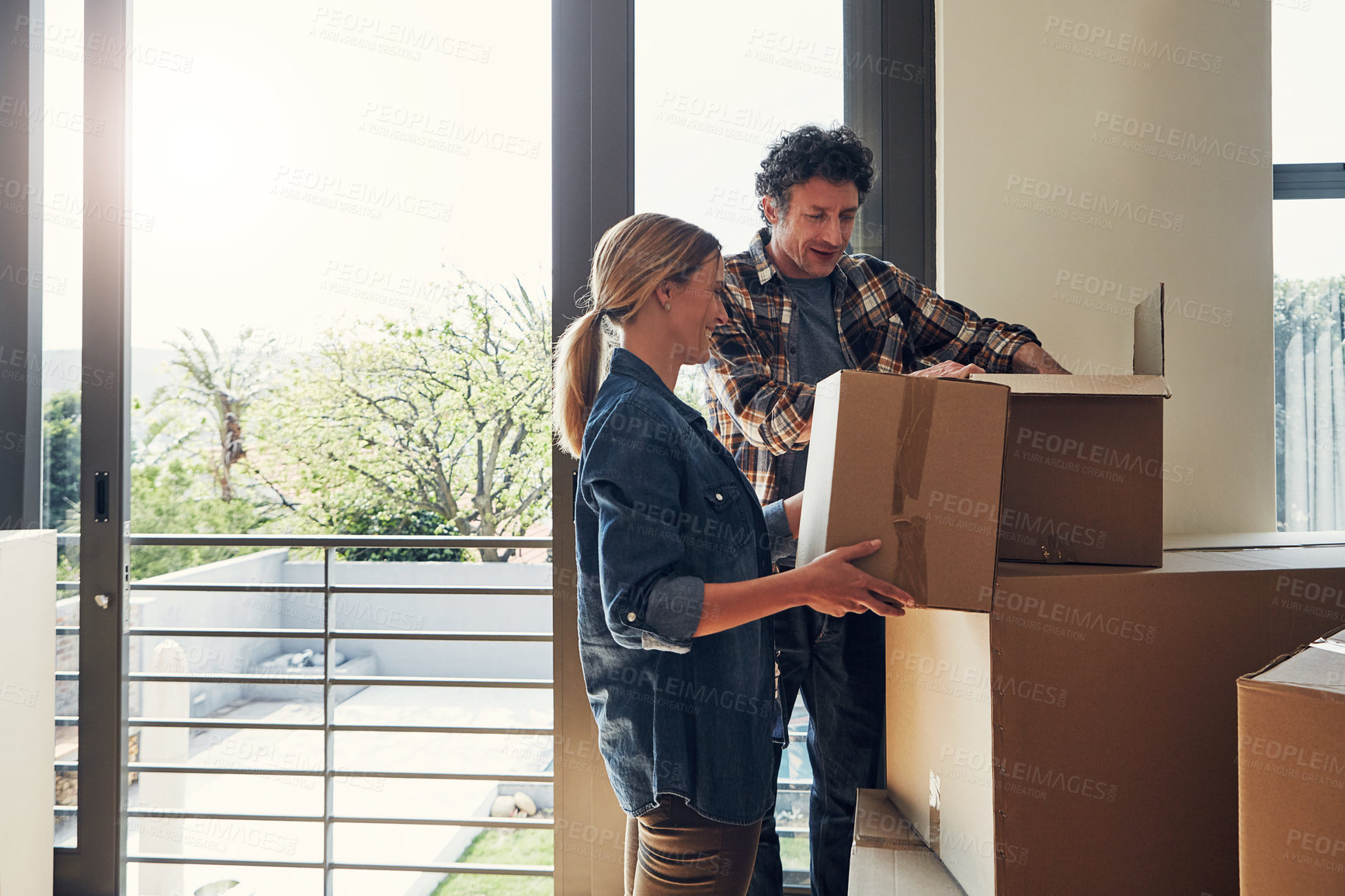 Buy stock photo Shot of a cheerful middle aged couple packing out a boxes at their new home inside during the day