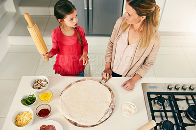 Buy stock photo High angle shot of a middle aged mother and her daughter preparing a pizza to go into the oven in the kitchen at home