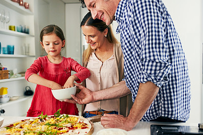 Buy stock photo Shot of a cheerful family preparing a pizza together to go into the oven in the kitchen at home