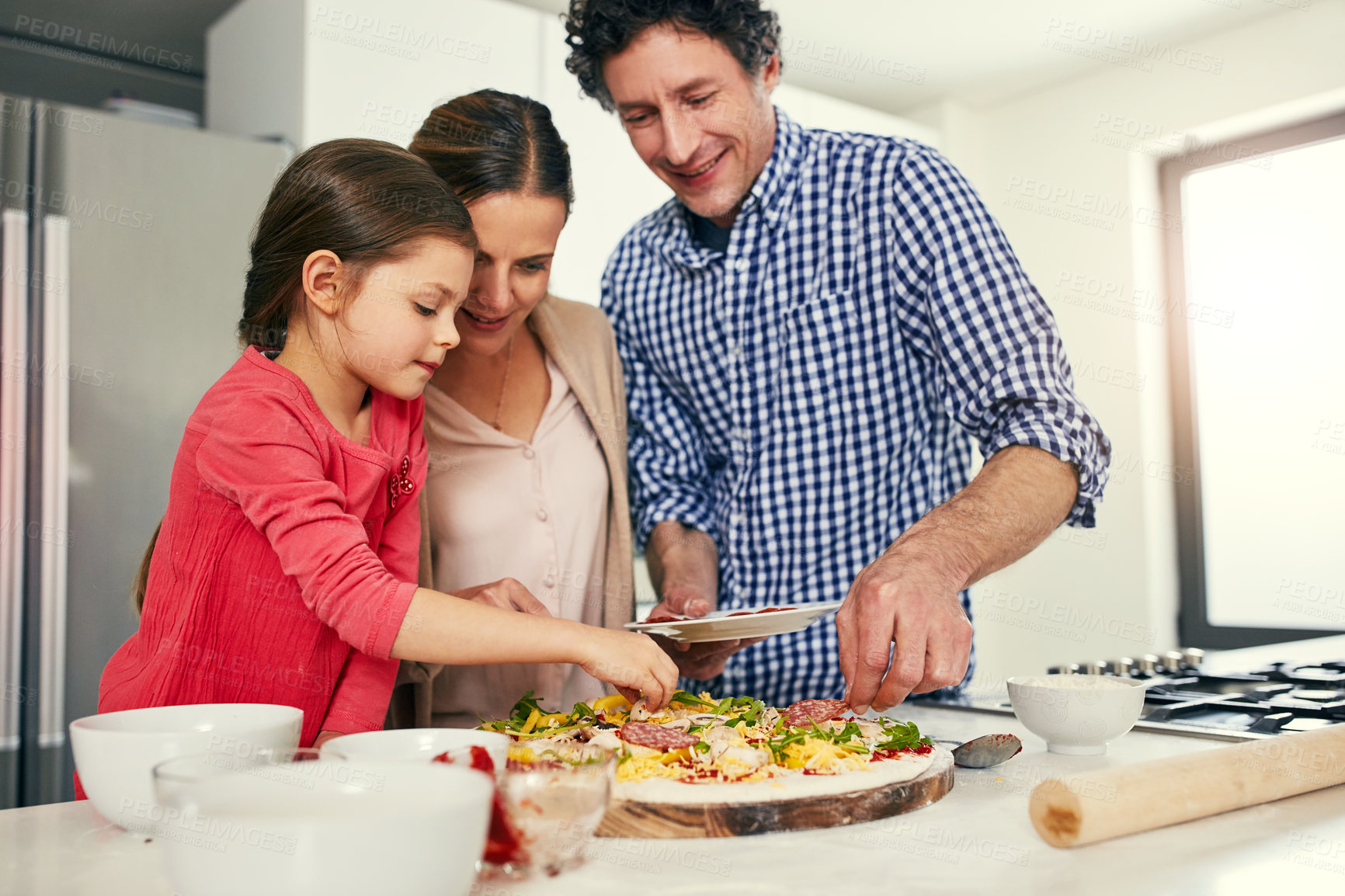 Buy stock photo Shot of a cheerful family preparing a pizza together to go into the oven in the kitchen at home