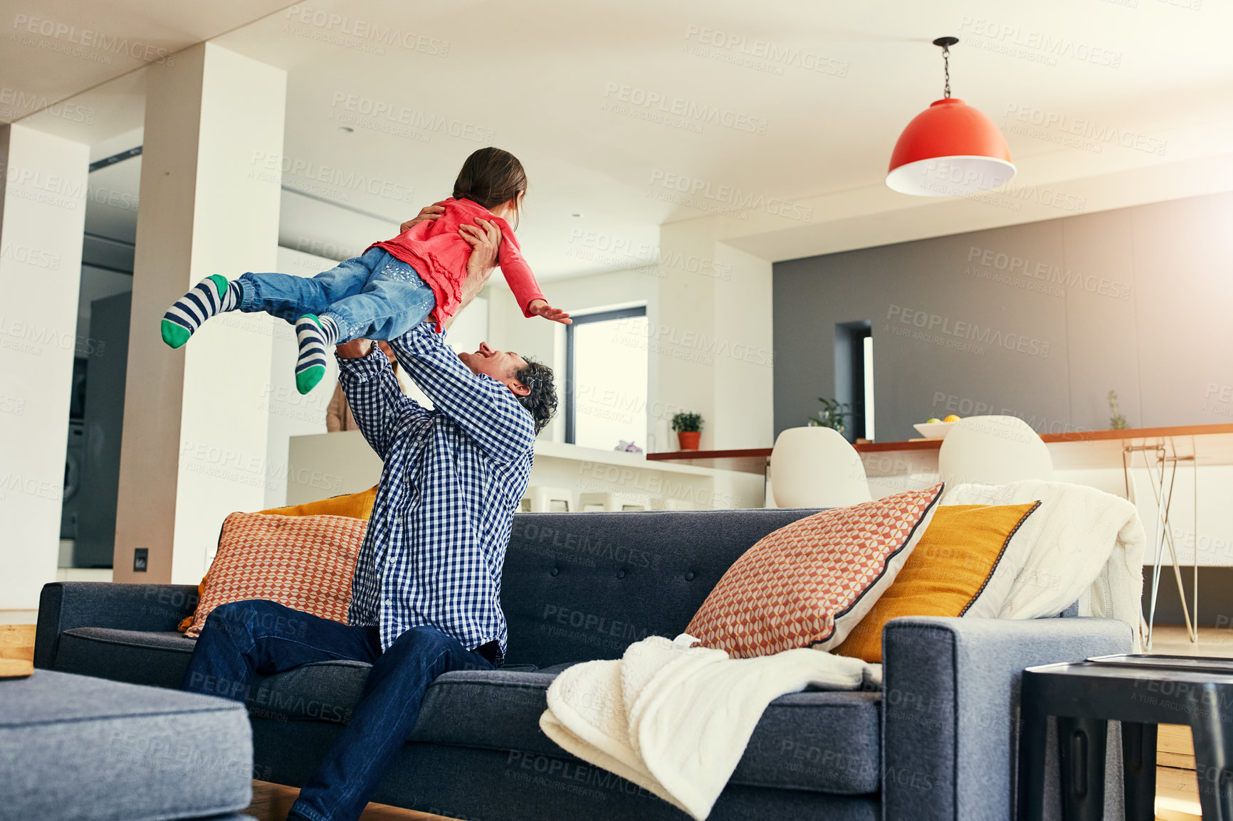 Buy stock photo Shot of a cheerful middle aged father holding his young daughter in the air while playing and being seated on the couch at home during the day