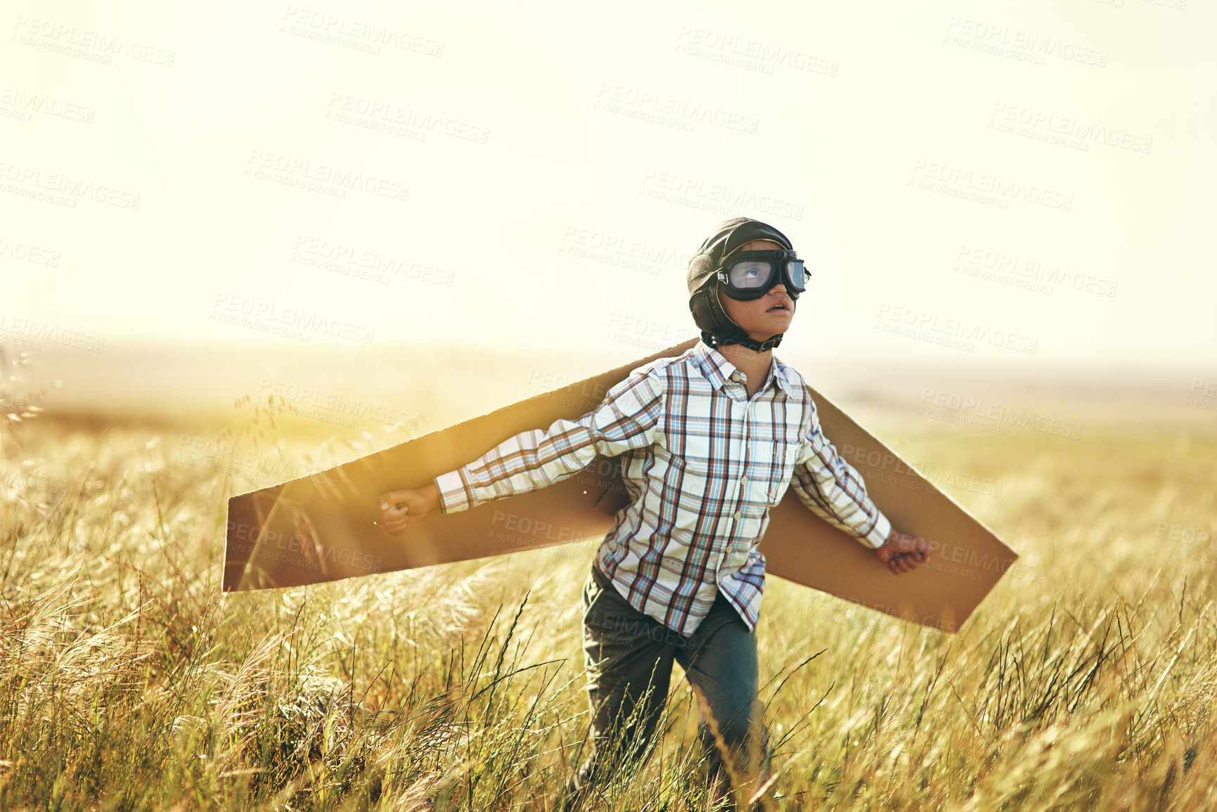 Buy stock photo Shot of a young boy pretending to fly with a pair of cardboard wings in an open field