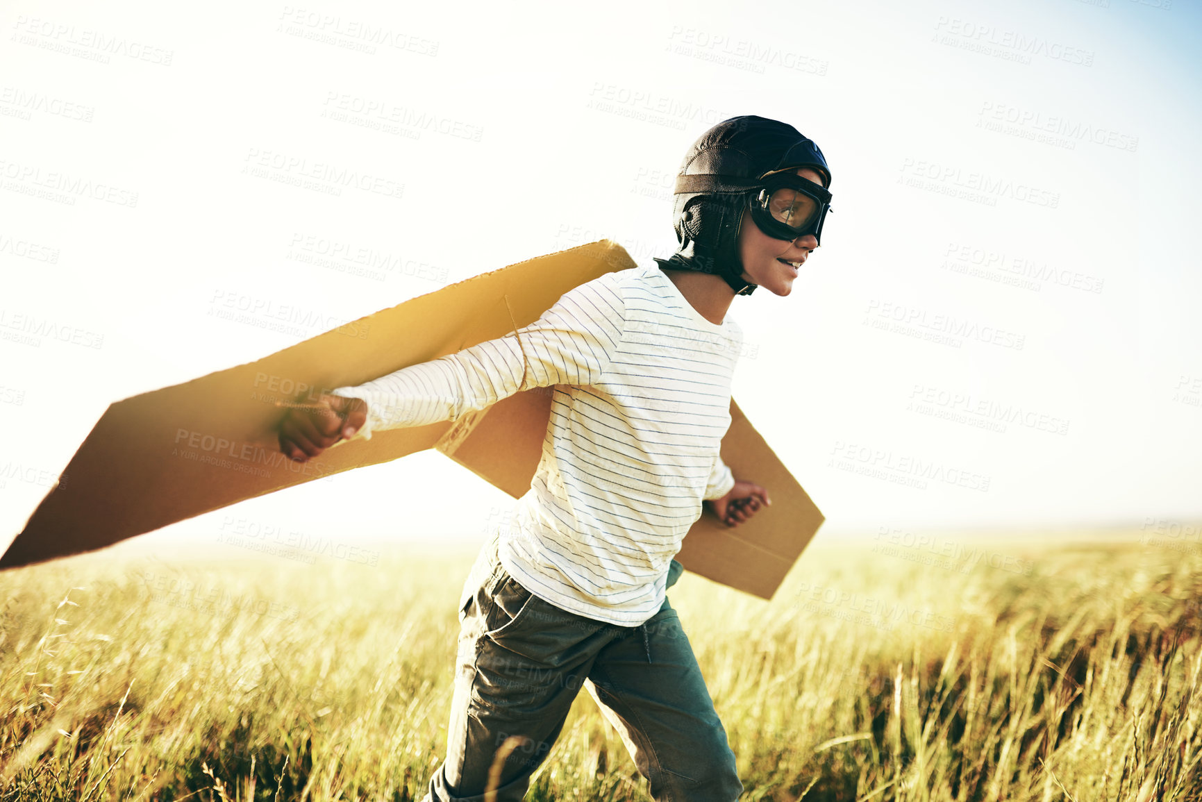 Buy stock photo Shot of a young boy pretending to fly with a pair of cardboard wings in an open field
